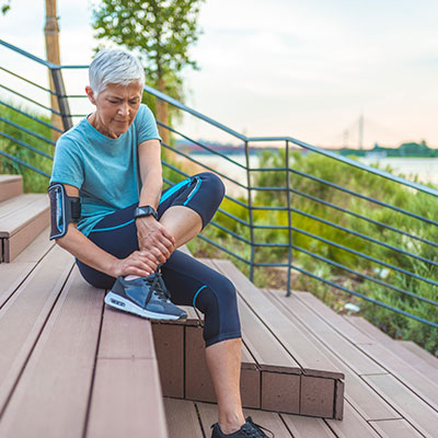 Older woman siting down holding her ankle in running gear