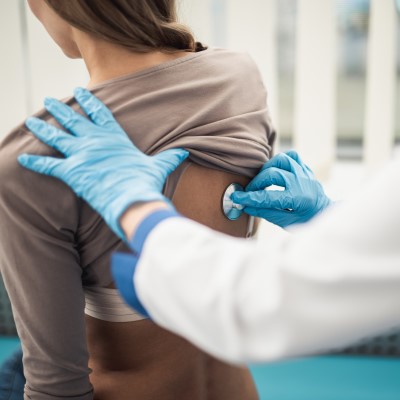 Doctor placing stethoscope on patients back 